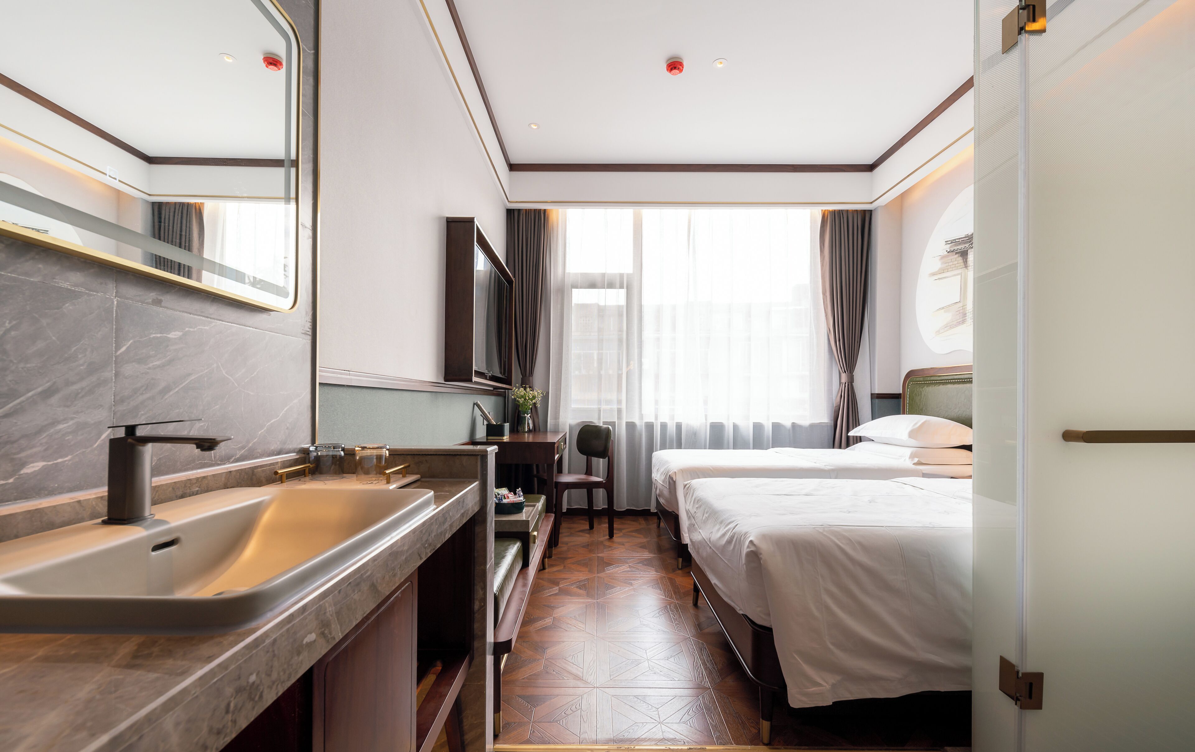 A modern hotel room with a bathroom, a bed, and a desk.
