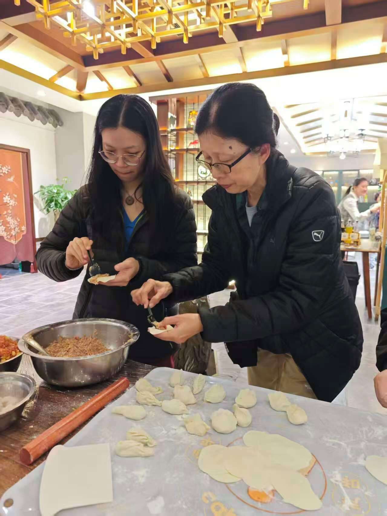 Deux personnes préparent des aliments, avec un saladier d’ingrédients et de la pâte sur la table.