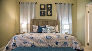 Un dormitorio con una cama, dos mesitas de noche, un banco y una pared con cuatro cuadros enmarcados.