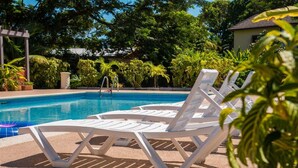 Un área junto a la piscina con sillas reclinables blancas y una piscina de color azul claro.