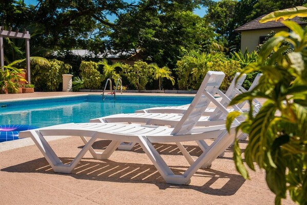 A poolside area with white lounge chairs and a clear blue pool.