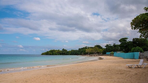 Una playa con arena, cielo despejado y una pequeña isla a lo lejos.