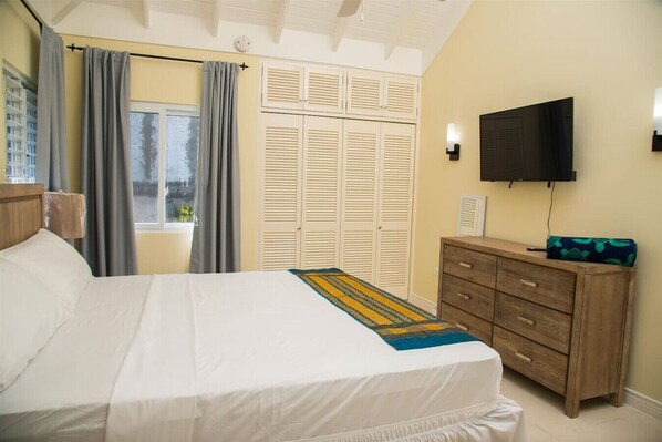 Una habitación de hotel con cama, tocador de madera, televisor y ventana con cortinas.