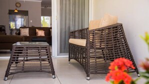 A wicker sofa with cushions and a matching ottoman in a modern living room with a glass table. - EN CASA @ Richmond Estate (Priory)