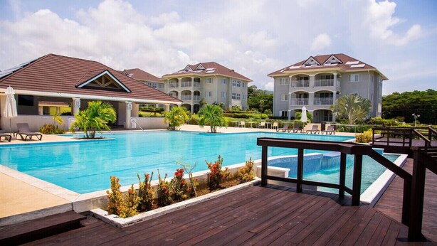 A swimming pool with a wooden deck, surrounded by buildings with balconies and a clear sky. - EN CASA @ Richmond Estate (Priory)