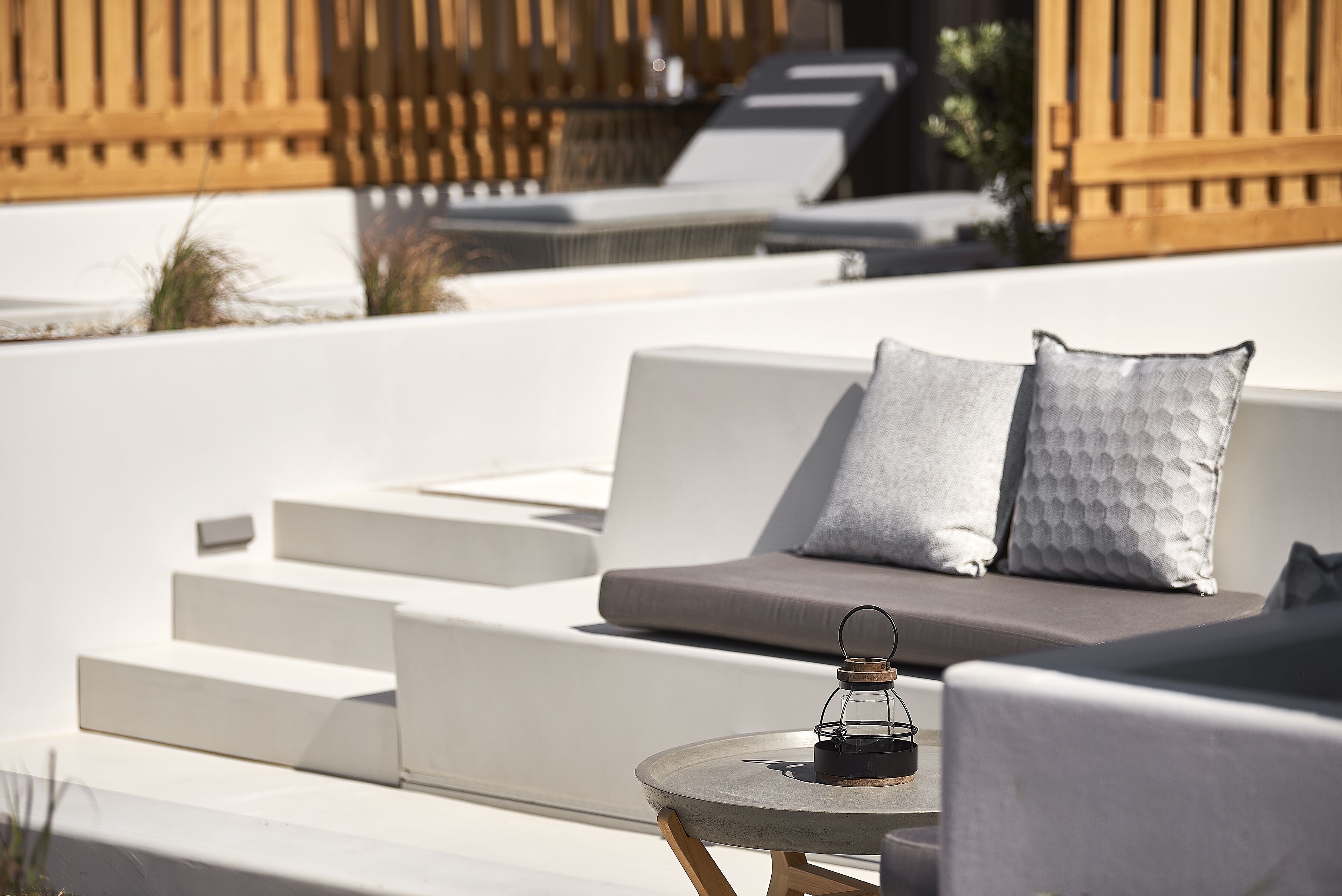 A modern outdoor seating area with a cushioned sofa, a small round table, and a lantern.