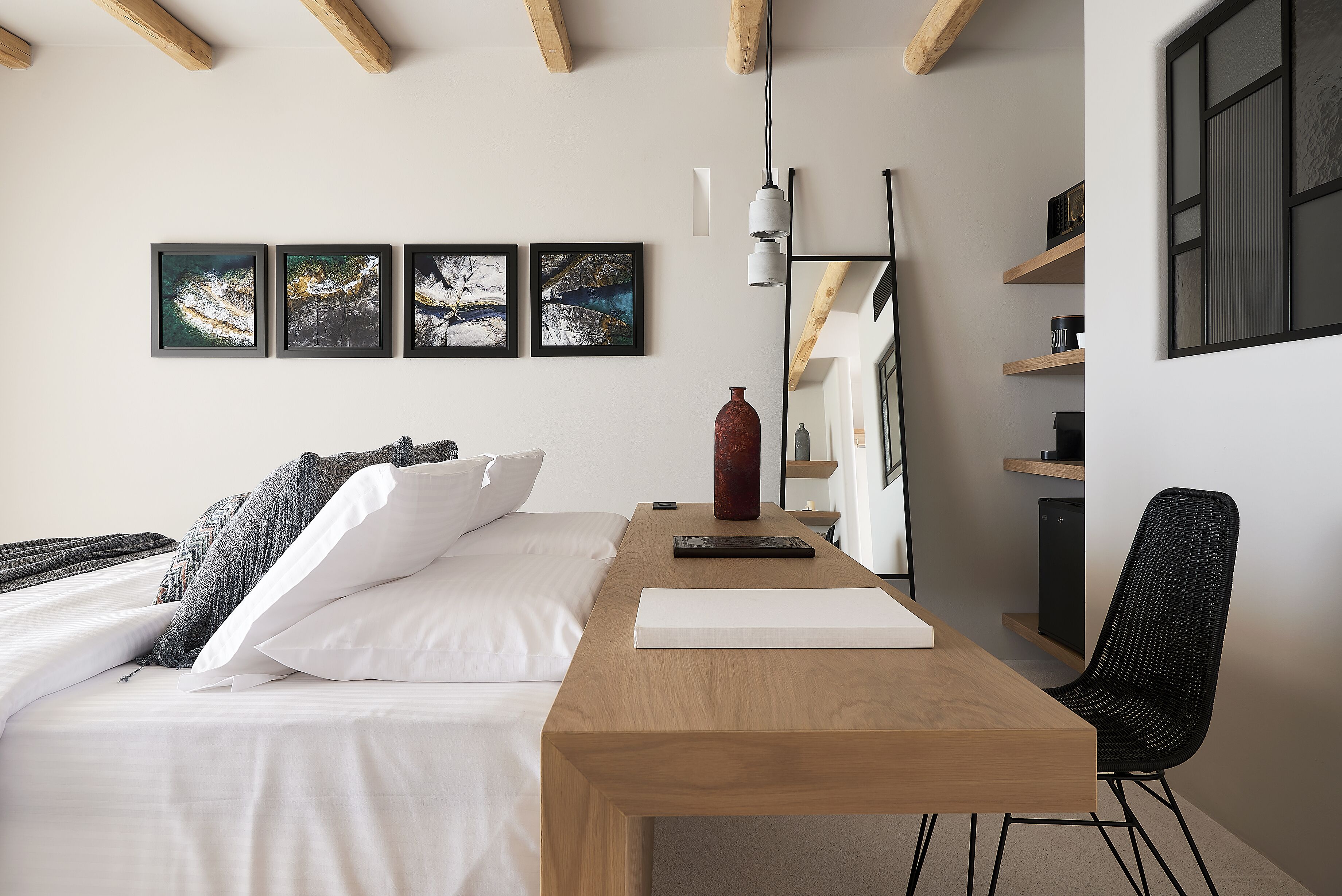 A modern hotel room with a wooden bed, white bedding, a wooden desk, a black chair, and three framed pictures on the wall.