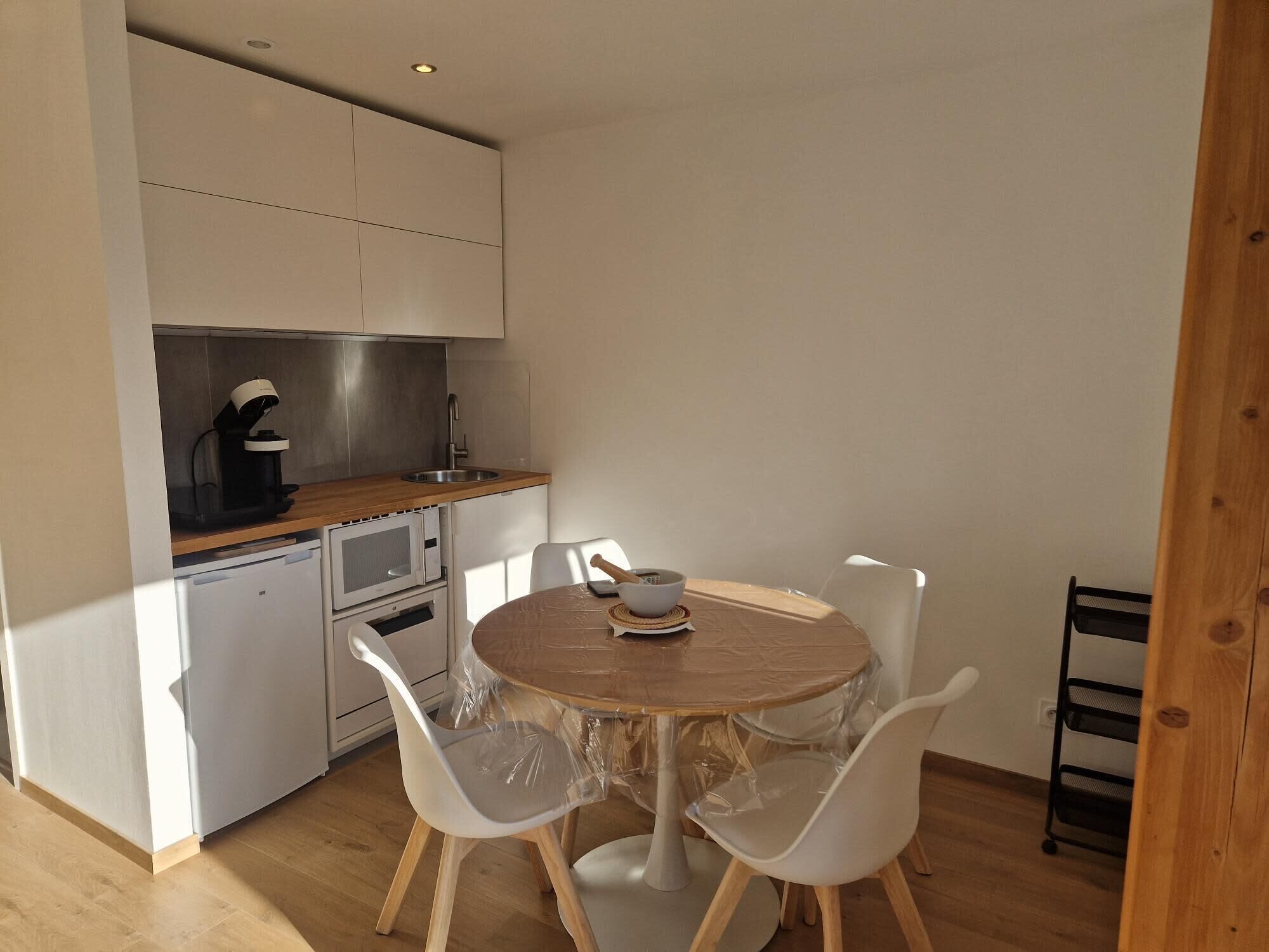 Een compacte keuken met een houten aanrecht, een spoelbak en een koffiezetapparaat. Er staan twee witte stoelen rond een klein rond tafeltje.