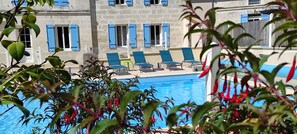 A poolside area with blue chairs and a stone building with blue shutters in the background. - Appart'é Nature l'ESCALE - SAINTES (Chaniers)
