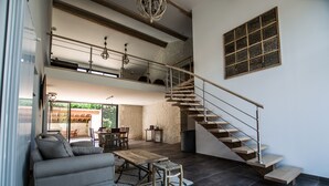 A spacious living area with a high ceiling, a wooden staircase, and a large window providing natural light. - Appart'é Nature l'ESCALE - SAINTES (Chaniers)