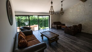 A spacious living room with a large window, a wooden coffee table, leather sofas, and hanging light fixtures. - Appart'é Nature l'ESCALE - SAINTES (Chaniers)