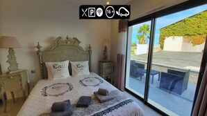 A hotel room with a large bed, two pillows with "Lau de" text, a nightstand with a lamp, and a view of the outside through a large window. - Appart'é Nature l'ESCALE - SAINTES (Chaniers)