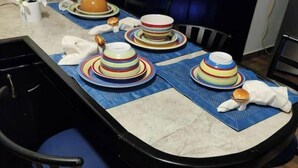 Une table à manger avec des assiettes rayées aux couleurs vives, un vase blanc rempli de fleurs et un pot marron.