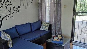 Un salon avec un canapé d’angle bleu, une petite table avec un plateau et un mur décoratif orné d’un motif représentant un arbre et un oiseau.