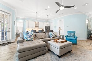 Uma sala de estar ampla com sofá seccional, banqueta e poltrona azul.