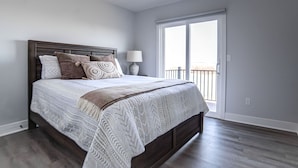 A bedroom with a large bed, a nightstand, a lamp, and a view of the outside balcony. - Quaint house on the bluffs overlooking the  scenic Missouri River. (Atchison)