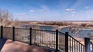 A wooden deck with a black metal railing overlooking a river. - Quaint house on the bluffs overlooking the  scenic Missouri River. (Atchison)
