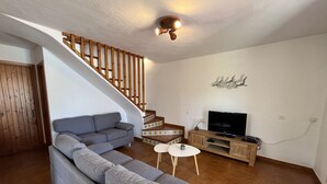 Un salon avec un canapé gris, un téléviseur posé sur un meuble en bois et un escalier doté d’une rampe en bois.