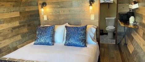 Un dormitorio con pared de madera, una cama con almohadas estampadas, una mesita de noche y un espejo.