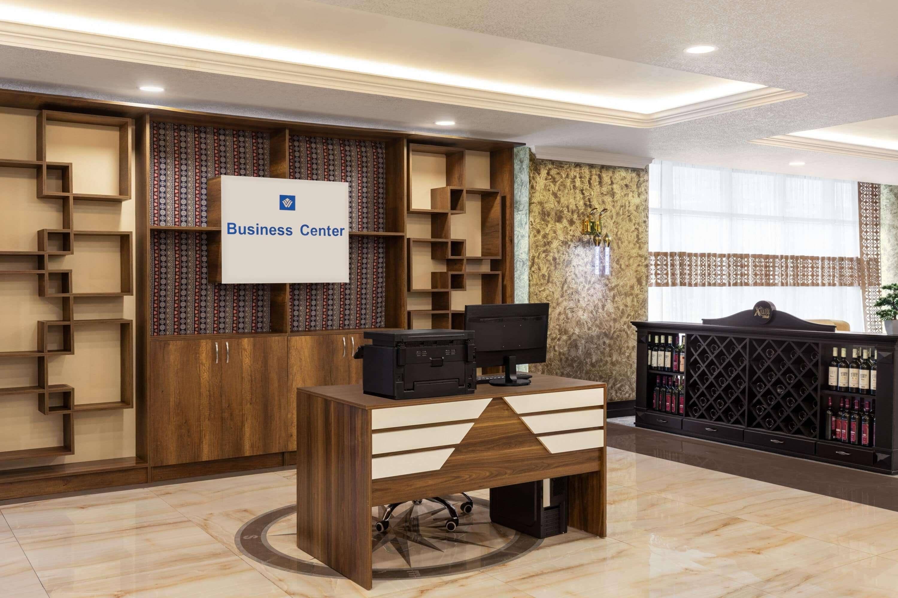 Un mostrador de recepción con un cartel que dice 'Business Center', una impresora y un enfriador de vino.