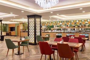A restaurant with multiple tables and chairs, a counter with food items, and a decorative wall with geometric patterns. - Wyndham Baku (Baku)