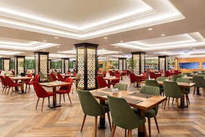 A spacious indoor dining area with multiple tables and chairs, decorative pillars, and a modern ceiling design.
