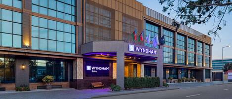A modern hotel building with large windows, a prominent entrance, and flags.