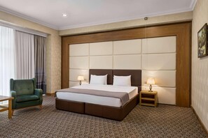 A hotel room with a large bed, a green armchair, two bedside tables with lamps, and a patterned carpet. - Wyndham Baku (Baku)