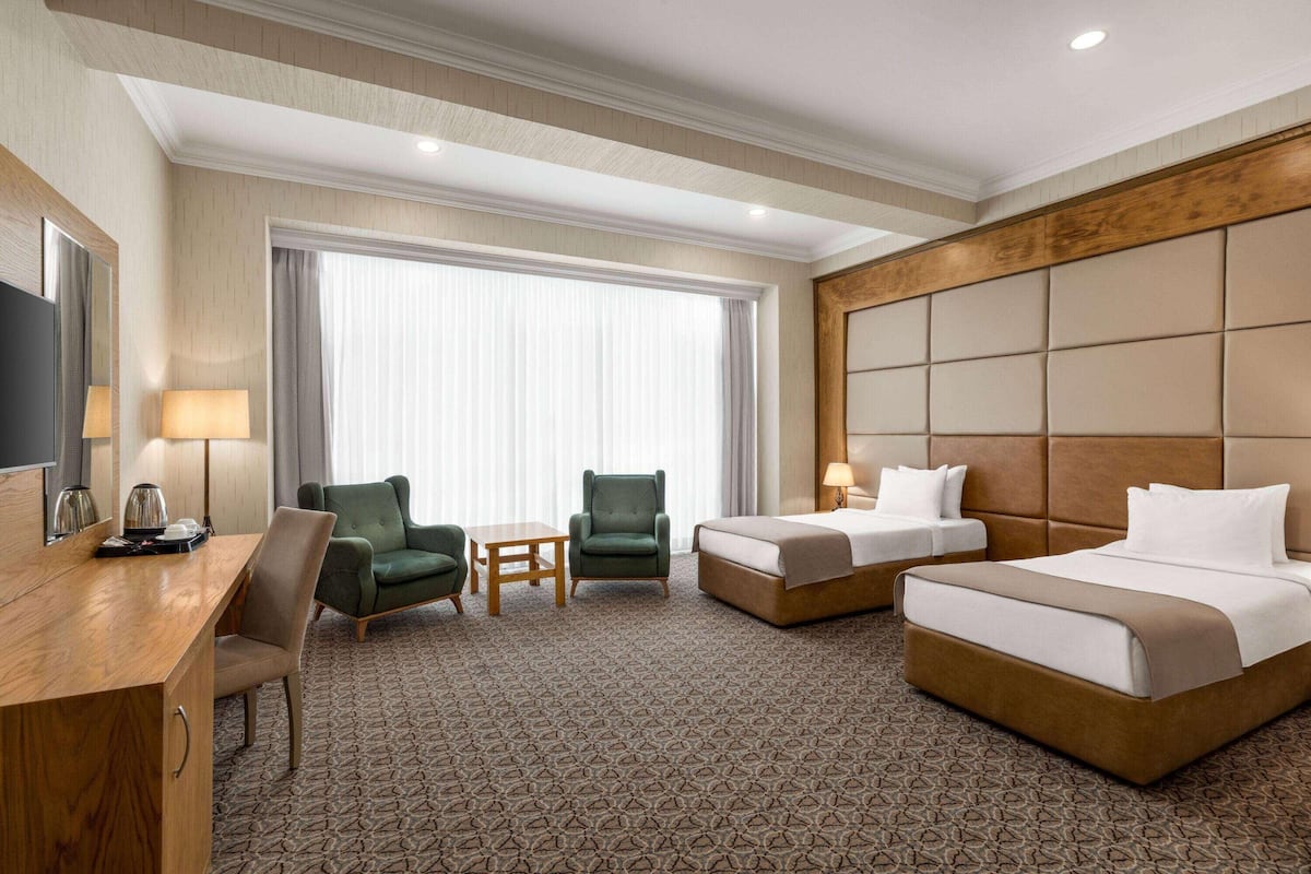 A hotel room with a bed, two armchairs, a desk, a TV, and a large window with curtains.