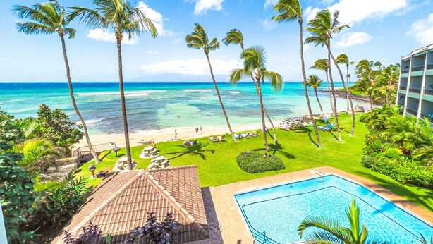 A poolside view with a clear view of the ocean and beach, surrounded by palm trees and a building. - Oceanfront | Walk to Beach  | Hale Mahina B305 | (Lahaina)