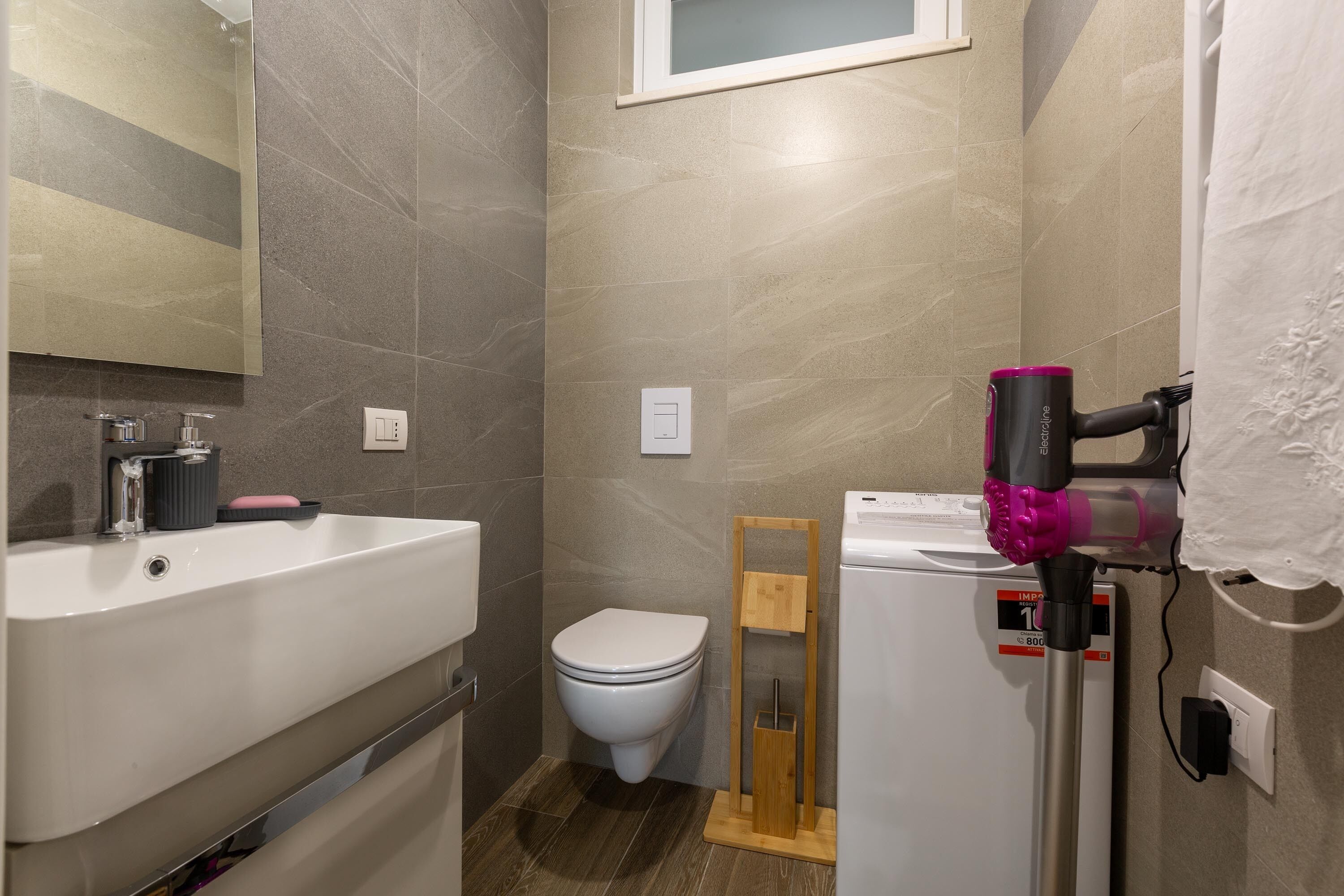 Een moderne badkamer met een wit wastafelmeubel, toilet en een haardroger op een standaard.