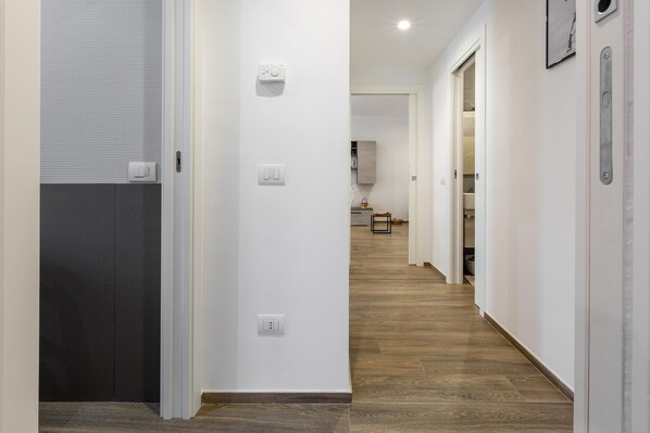 Un pasillo con suelo de madera, paredes blancas y una puerta que da a una habitación.