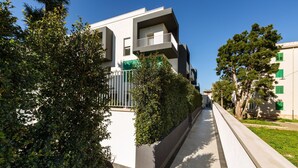 Un moderno edificio de apartamentos con balcones, un sendero pavimentado y árboles verdes.