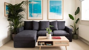 Un salon moderne avec un canapé d’angle, une table basse et deux œuvres d’art encadrées accrochées au mur.