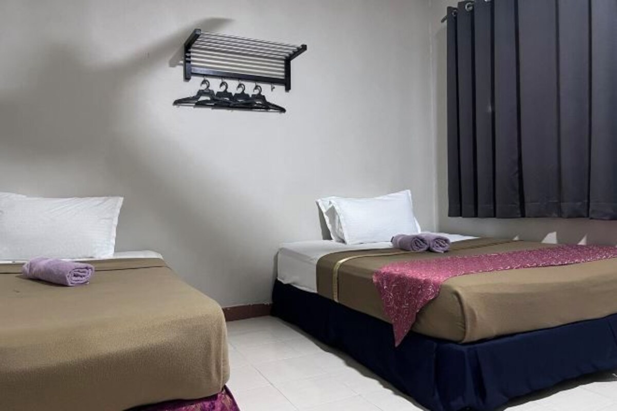 Hotellihuone, jossa on kaksi sänkyä, ja jokaisessa on erivärinen peitto, seinälle kiinnitetty naulakko ja ikkuna, jossa on verhot.