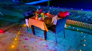 An outdoor dining area with a table set for two, surrounded by candles and scattered rose petals. - Capital O 91017 Tuba Beach Resort @ Pulau Tuba (Pulau Tuba)
