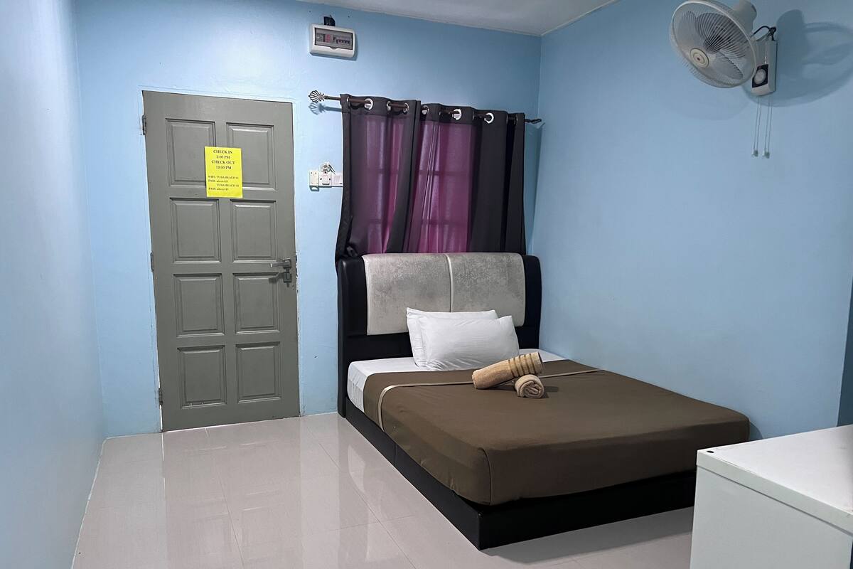 A bedroom with a bed, a door, a wall-mounted fan, and a thermostat.