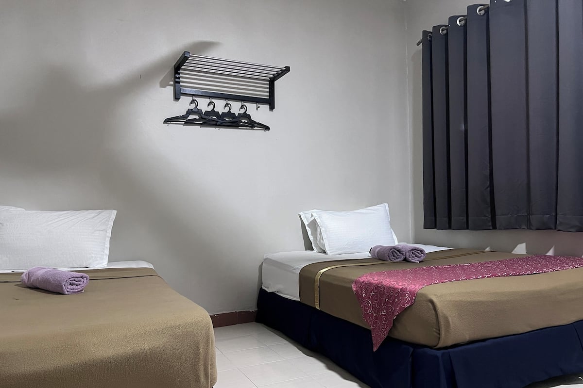 A hotel room with two beds, each with a duvet and pillows, a towel on the floor, a radiator, and a wall-mounted towel rack.