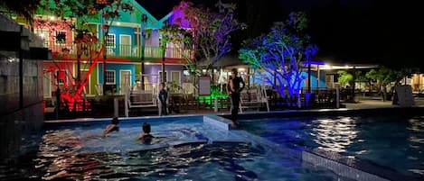 Ein Schwimmbeckenbereich mit Blick auf bunte Gebäude im Hintergrund bei Nacht.