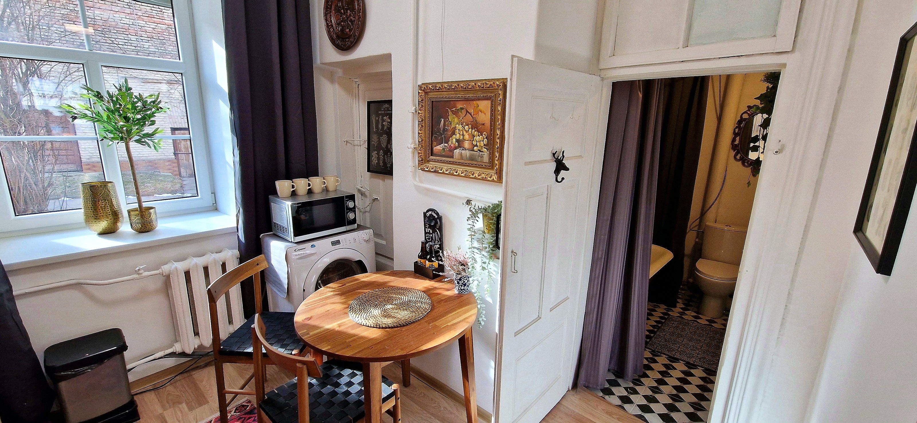 A compact kitchen with a microwave, a washing machine, and a small dining table with a chair.