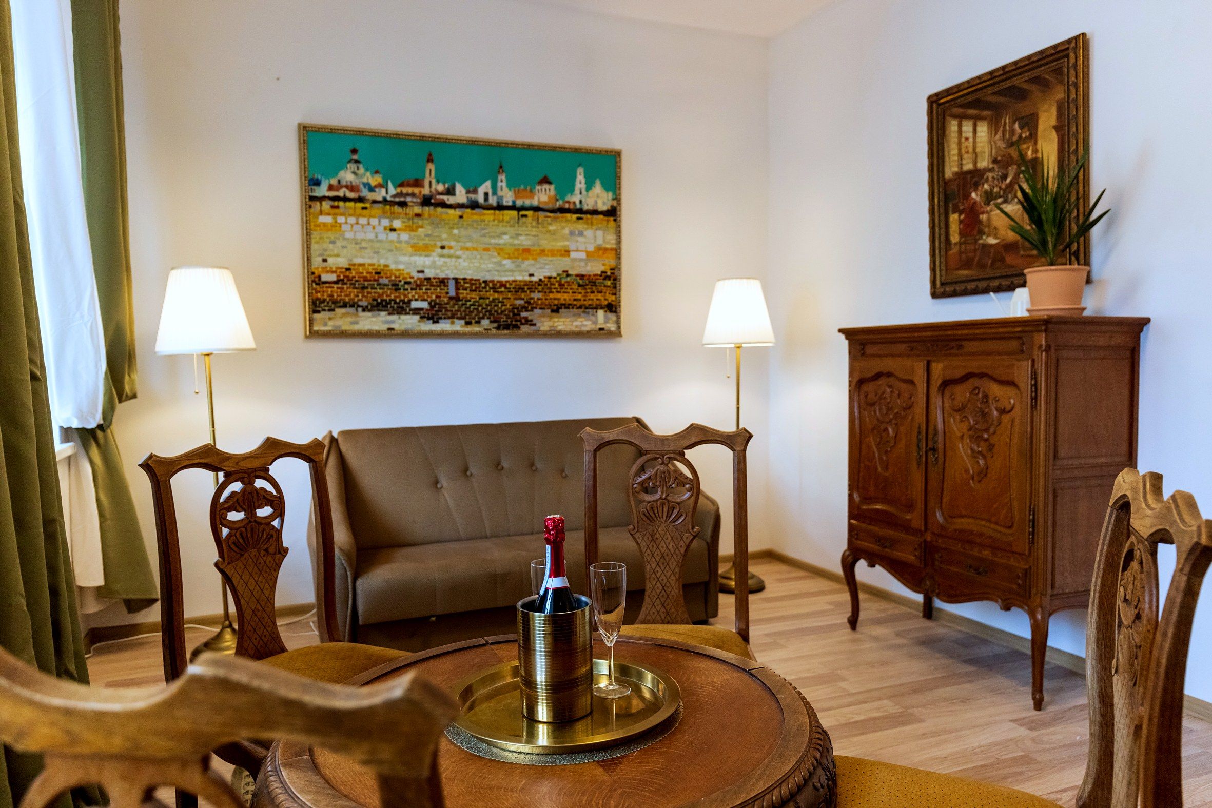 Uma sala de estar com um sofá, duas luminárias, um quadro, um aparador e uma garrafa de champanhe em um suporte.