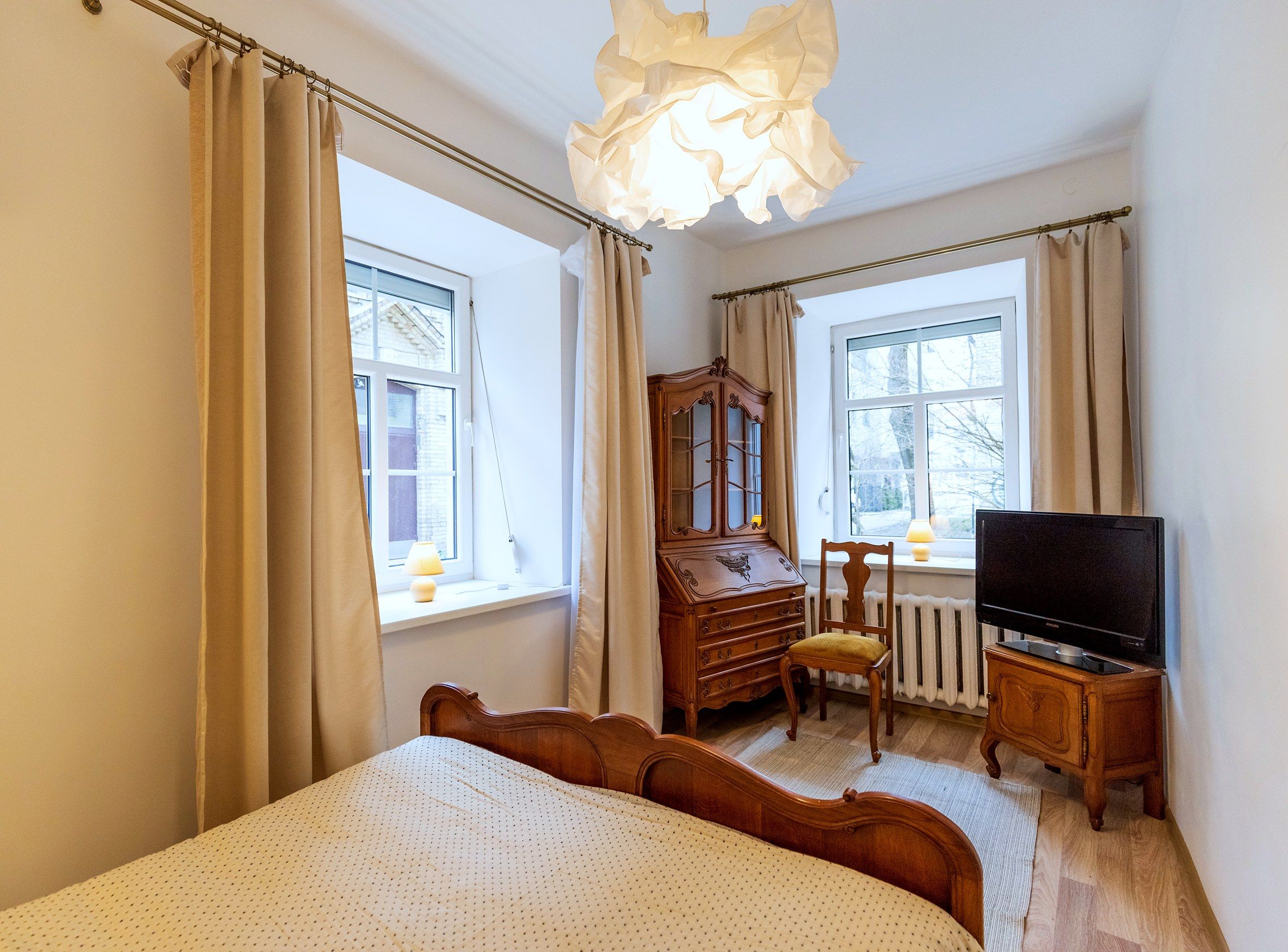 A bedroom with a bed, a wooden dresser, a chair, a television, and a window.
