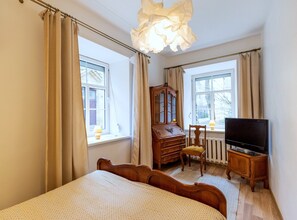 Un dormitorio con cama, cómoda de madera, silla, televisor y ventana.