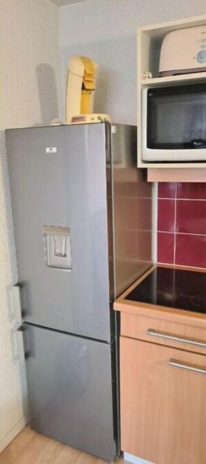 A compact kitchen with a stainless steel refrigerator, a microwave, and wooden cabinets.