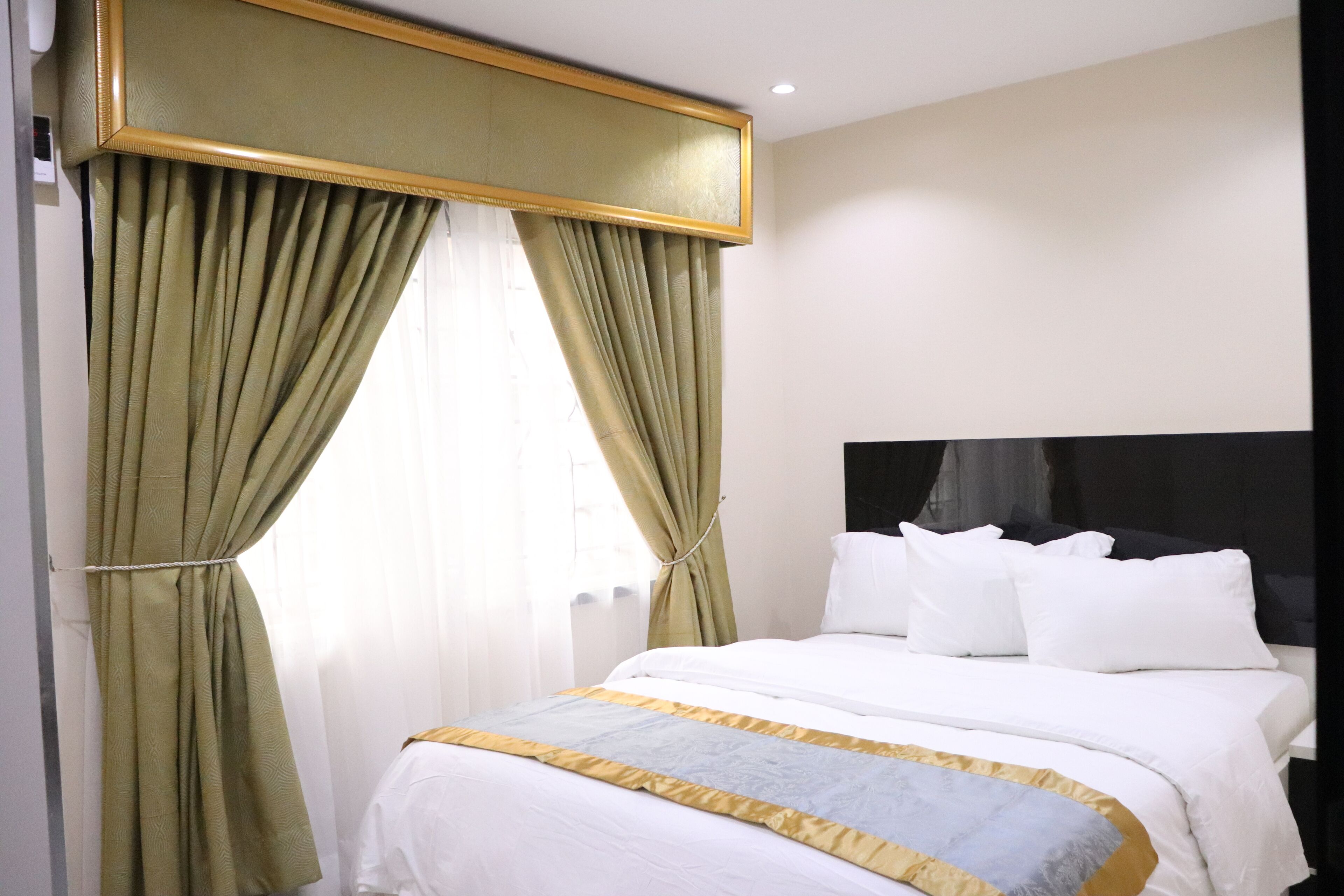 A hotel room with a large bed, green curtains, white bedding, and a black headboard.