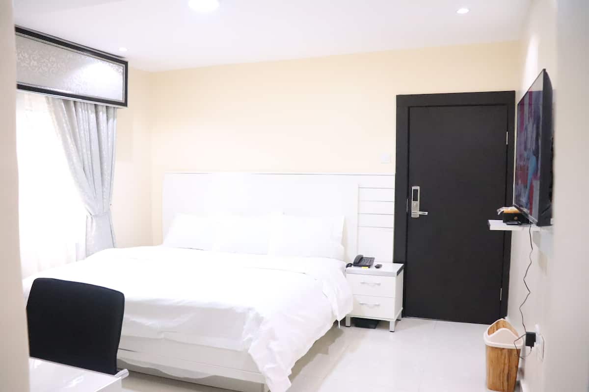 A hotel room with a bed, bedside table, chair, and a door.