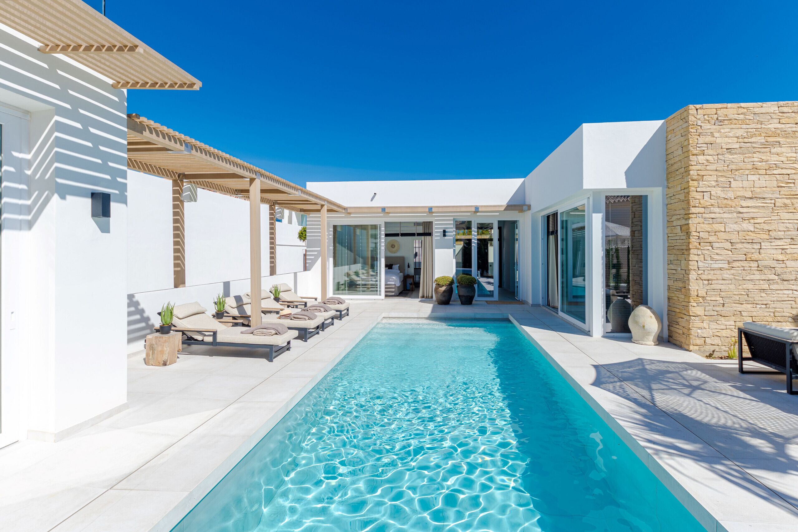 Uma área de piscina moderna com piscina azul cristalina, espreguiçadeiras e um muro de pedra.