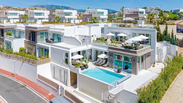 Un complejo residencial moderno con varias casas de dos pisos, una piscina central y vistas del paisaje circundante.