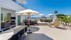 Una terraza iluminada por el sol con una mesa y sillas de madera, rodeada de sombrillas blancas y plantas en macetas.