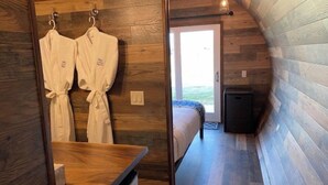 A cozy, wood-paneled room with a bed, a small table, and two robes hanging on hooks. - Riesling  Cabin (Seguin)